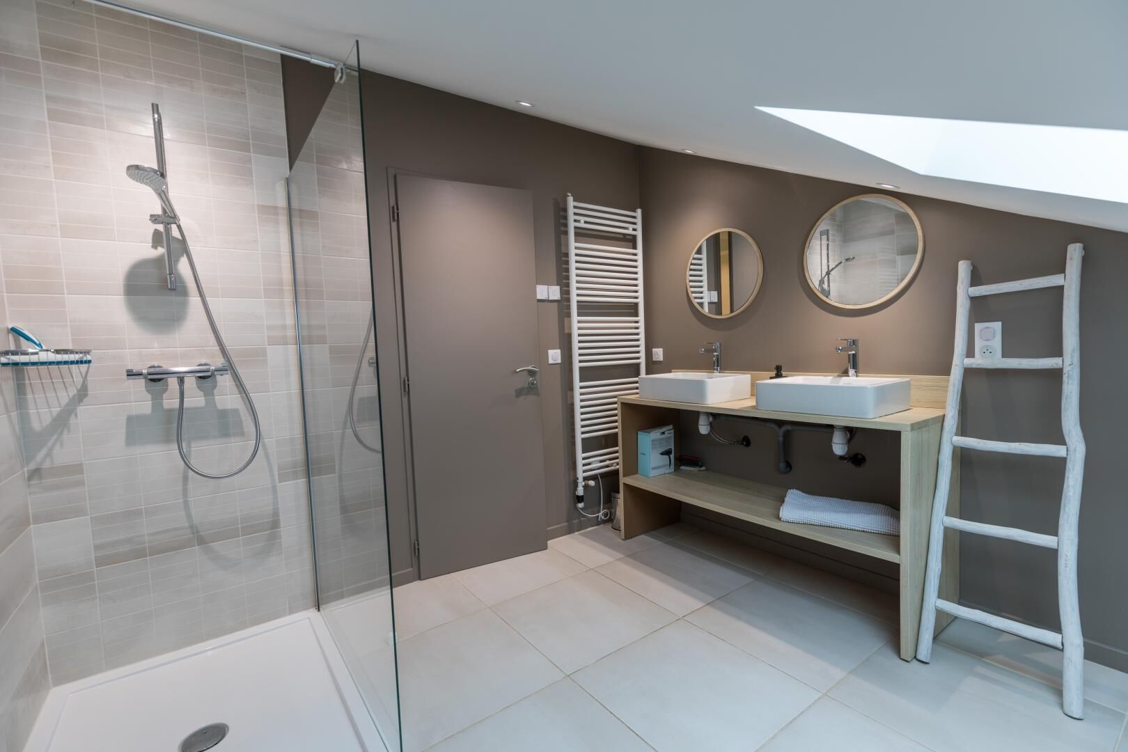 Une salle de bain moderne avec une douche à parois de verre, deux lavabos, un meuble-lavabo et un porte-serviettes échelle.