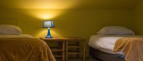 A small, dimly lit room with two beds, a small table, and a single lamp.