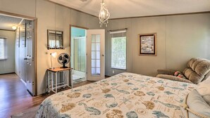 Een slaapkamer met een groot bed, een kroonluchter, een bureau met een ventilator en een deur naar een andere kamer.
