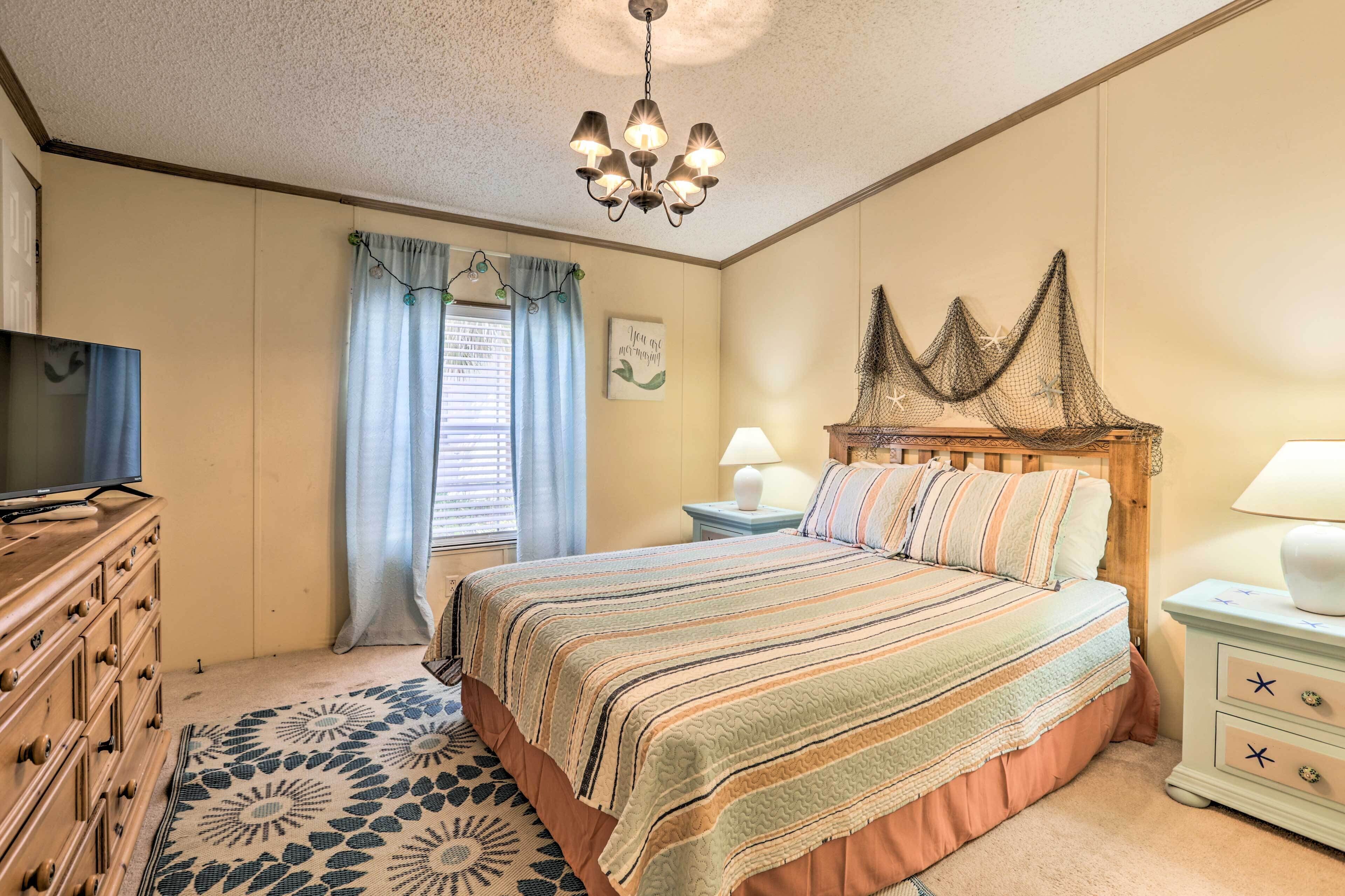 A bedroom with a bed, dresser, nightstand, lamp, and a chandelier.