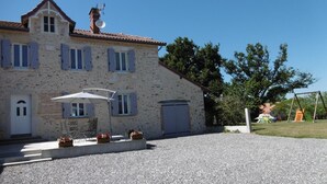 Un bâtiment en pierre avec un toit en tuiles, un patio couvert et une allée gravillonnée.