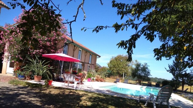 Une maison avec une piscine, des meubles de jardin et des plantes en pot.