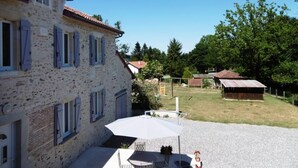 Un bâtiment en pierre avec un toit en tuiles, un espace extérieur abrité avec des sièges et une cour recouverte de gravier.