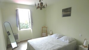 Une chambre à coucher comprenant un lit, un luminaire suspendu, une fenêtre avec des rideaux, une table de chevet et un tableau accroché au mur.