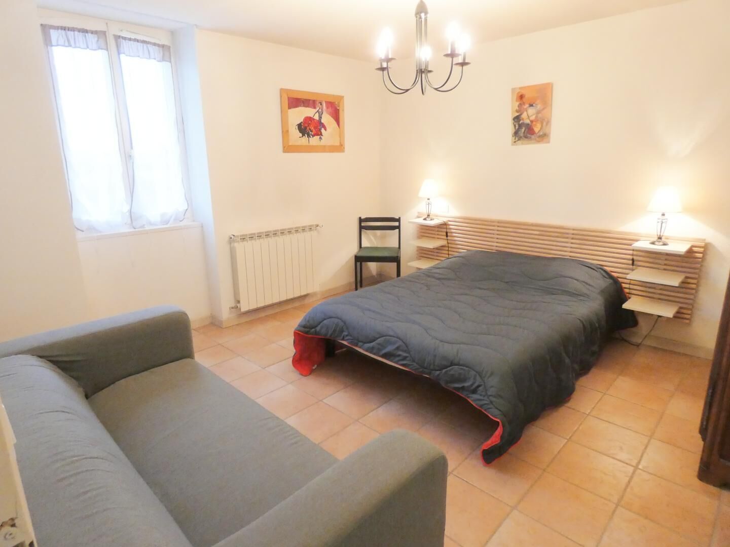 Ein Schlafzimmer mit einem Bett, einem Sessel, einem Heizkörper, einem Fenster und einer Chandelier.