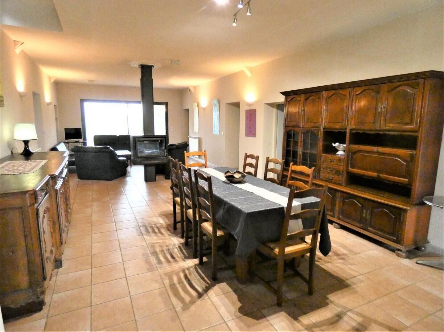 A dining area with a table set for four, surrounded by wooden chairs. A television is mounted on the wall, and a cabinet with multiple drawers is visible to the right.