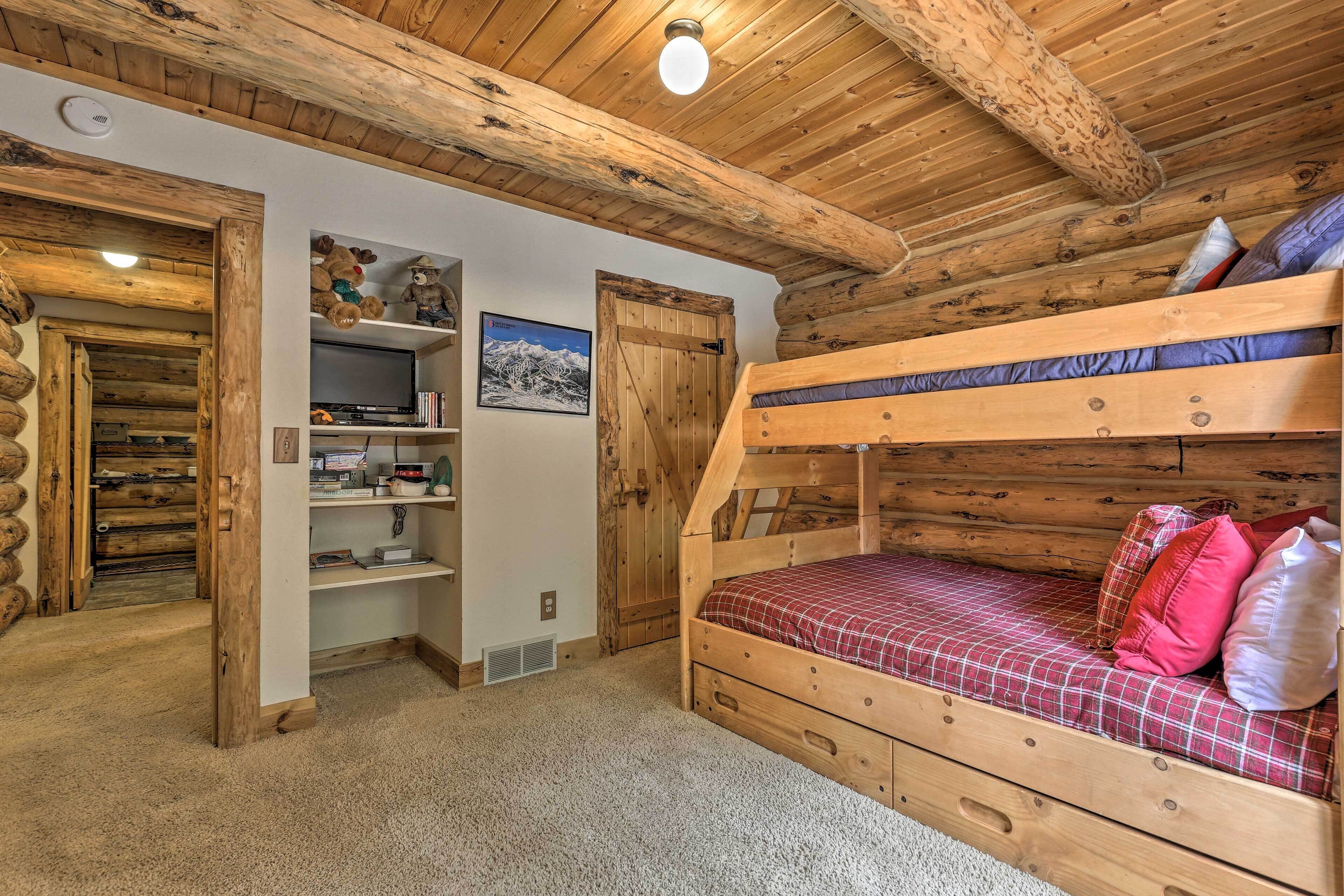 Una camera in baita di legno con un letto a castello, mensole di legno, una porta e un quadro appeso al muro.