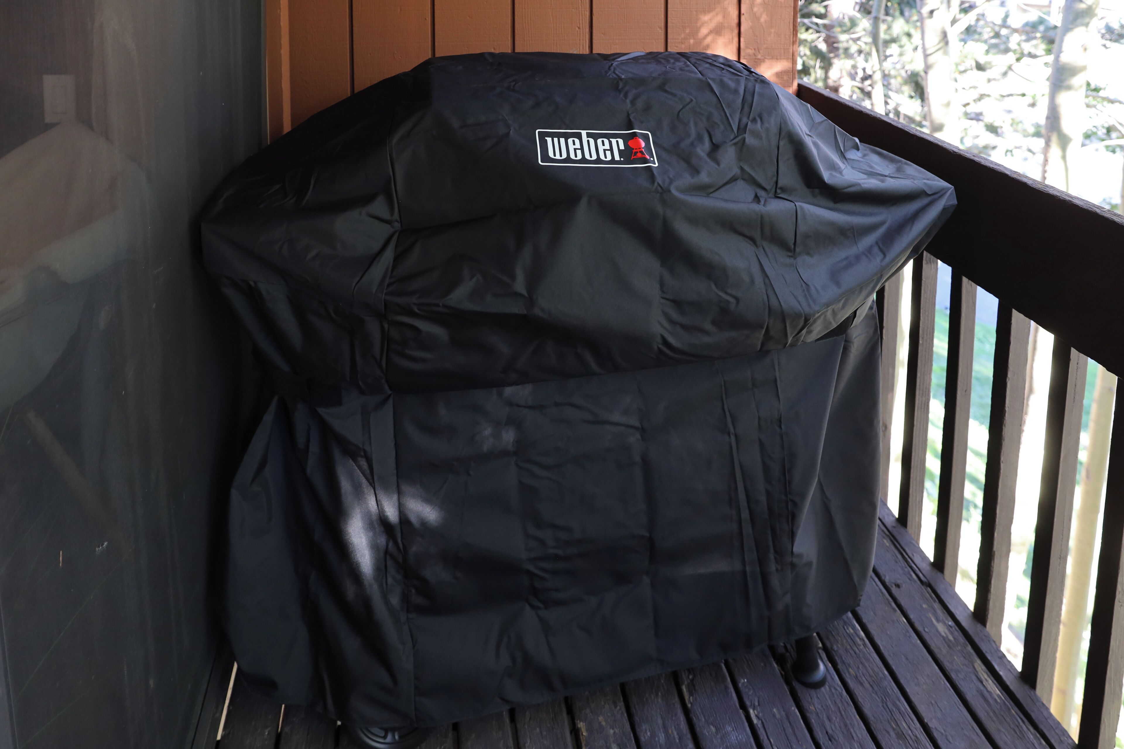 A covered barbecue grill with a logo on the side, placed on a wooden deck.