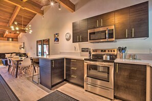 A modern kitchen with dark wood cabinets, stainless steel appliances, and a dining area with a wooden ceiling. - Contemporary Mountain Retreat - Walk to Slopes! (Mammoth Lakes)