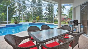 En uteplats med en pool som är inbyggd i en glasstruktur, möbler i rotting och en grill.