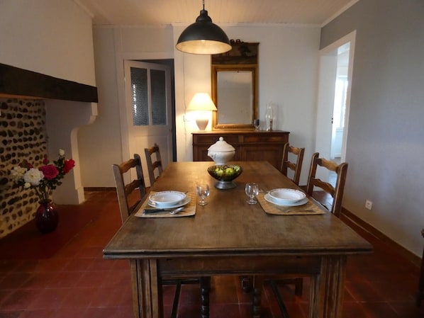 A dining room with a wooden table set for four, a bowl of fruit, and a lamp on the wall.