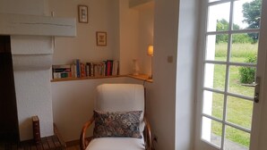 A cozy room with a fireplace, a bookshelf, a comfortable chair, and a large window offering a view of the outdoors.