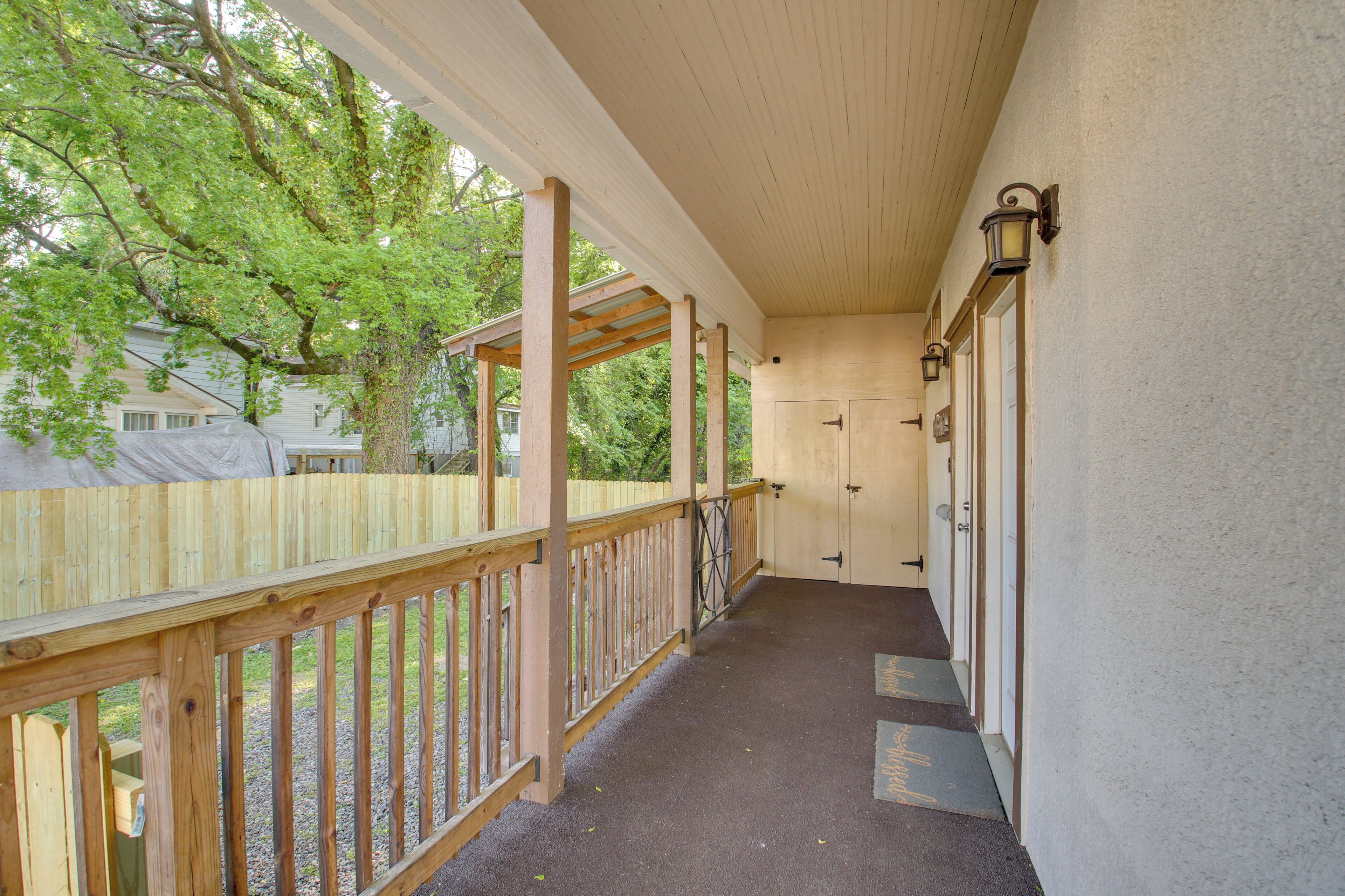 A covered porch with a wooden railing, a concrete floor, and a view of a tree and a house in the background.