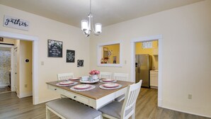 Een eethoek met een houten tafel voor zes personen, witte stoelen, een kroonluchter en wanddecoraties.