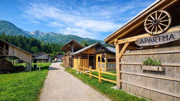 A wooden building labeled 'APARTMA' with a dirt path leading to it, surrounded by greenery and mountains. - Cozy Alpine Apartment near Lake Bohinj,  Free Bikes & No Extra Fees (Bohinjska Bistrica)