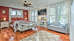 A bedroom with a bed, a nightstand, a dresser, a window, a ceiling fan, and a large window with a view of trees.