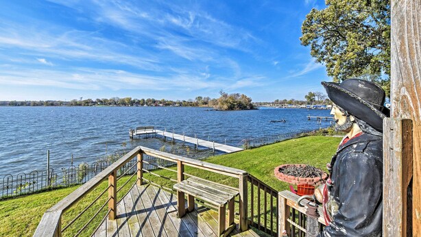 A wooden deck with a bench overlooking a lake, a statue of a historical figure, and a distant shoreline with boats.