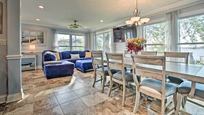 A spacious living room with a blue sofa, dining table with chairs, and a large window with a view of the outdoors.