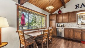 A kitchen with wooden cabinets, a dining table with chairs, a window with blinds, and a hanging light fixture. - 1 Mi to Slopes: Big Bear Ski Haven w/ Hot Tub (Big Bear Lake)
