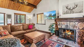 A cozy living room with a fireplace, a large sofa, and a stone wall. - 1 Mi to Slopes: Big Bear Ski Haven w/ Hot Tub (Big Bear Lake)