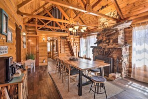 A rustic cabin interior with a wooden dining table, chairs, a fireplace, and a staircase leading to another room. - < 2 Mi to Lake: Big Bear City Cabin w/ Hot Tub! (Big Bear City)