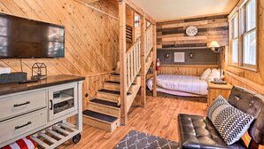 A wooden cabin interior with a TV, a sofa, a bed, and a staircase. - < 2 Mi to Lake: Big Bear City Cabin w/ Hot Tub! (Big Bear City)