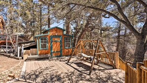 A wooden cabin with a porch and swing set, surrounded by trees. - < 2 Mi to Lake: Big Bear City Cabin w/ Hot Tub! (Big Bear City)