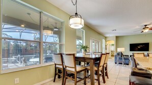 A spacious living room with a dining area, large windows, and a ceiling fan.