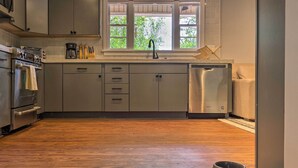 Cucina moderna con mobili grigi, un frigorifero in acciaio inossidabile e una finestra vista verde.