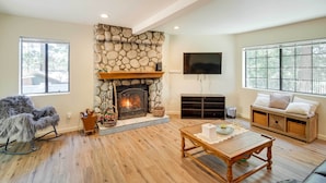 A living room with a stone fireplace, a flat-screen TV mounted on the wall, and a large window. - All-season Crestline Escape - 2 Mi to Lake! (Crestline)