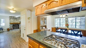 A spacious kitchen with wooden cabinets, a stone fireplace, and a large island with a gas stove. - All-season Crestline Escape - 2 Mi to Lake! (Crestline)