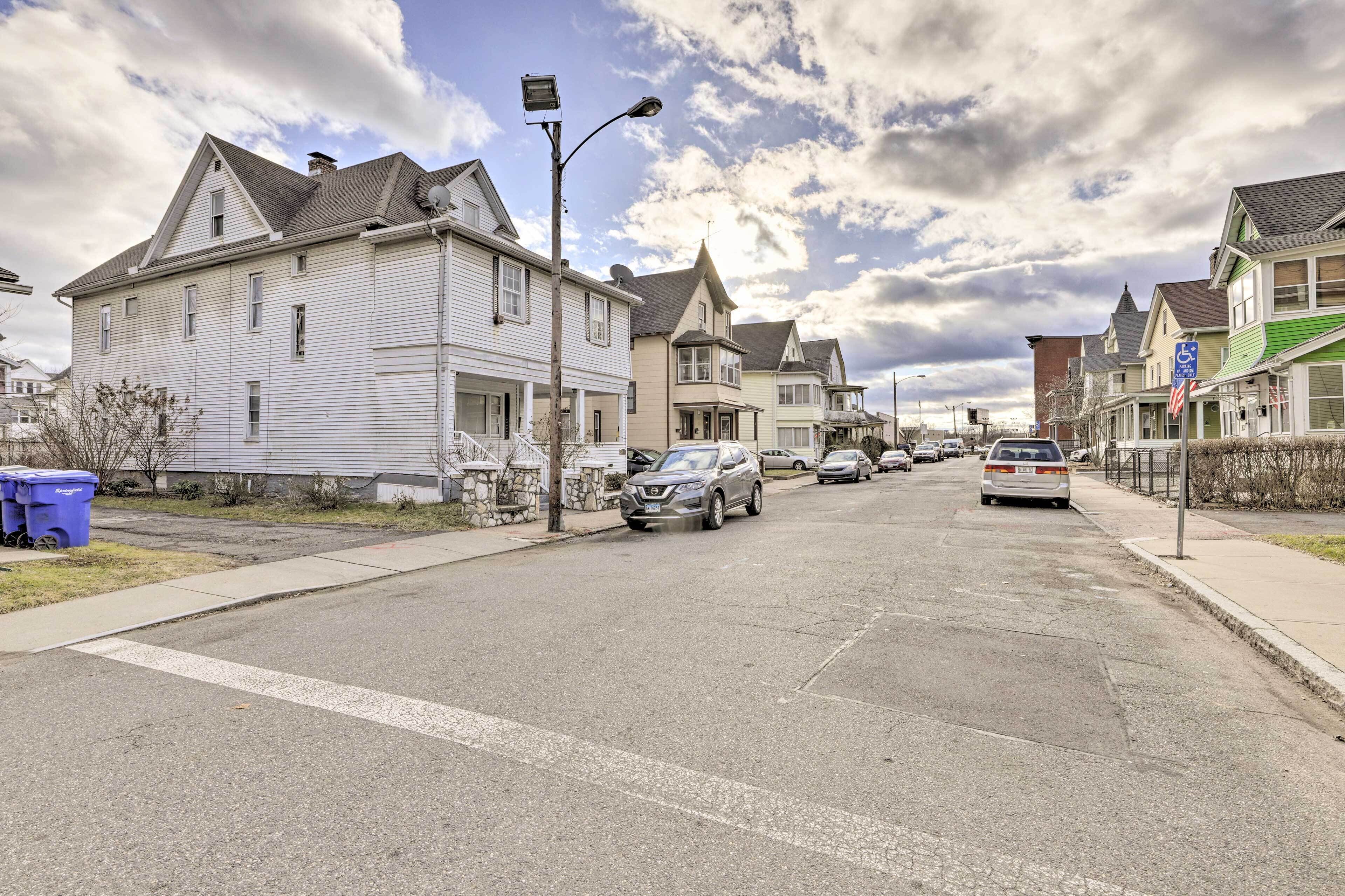 A residential street with houses, parked cars, and a clear sky.