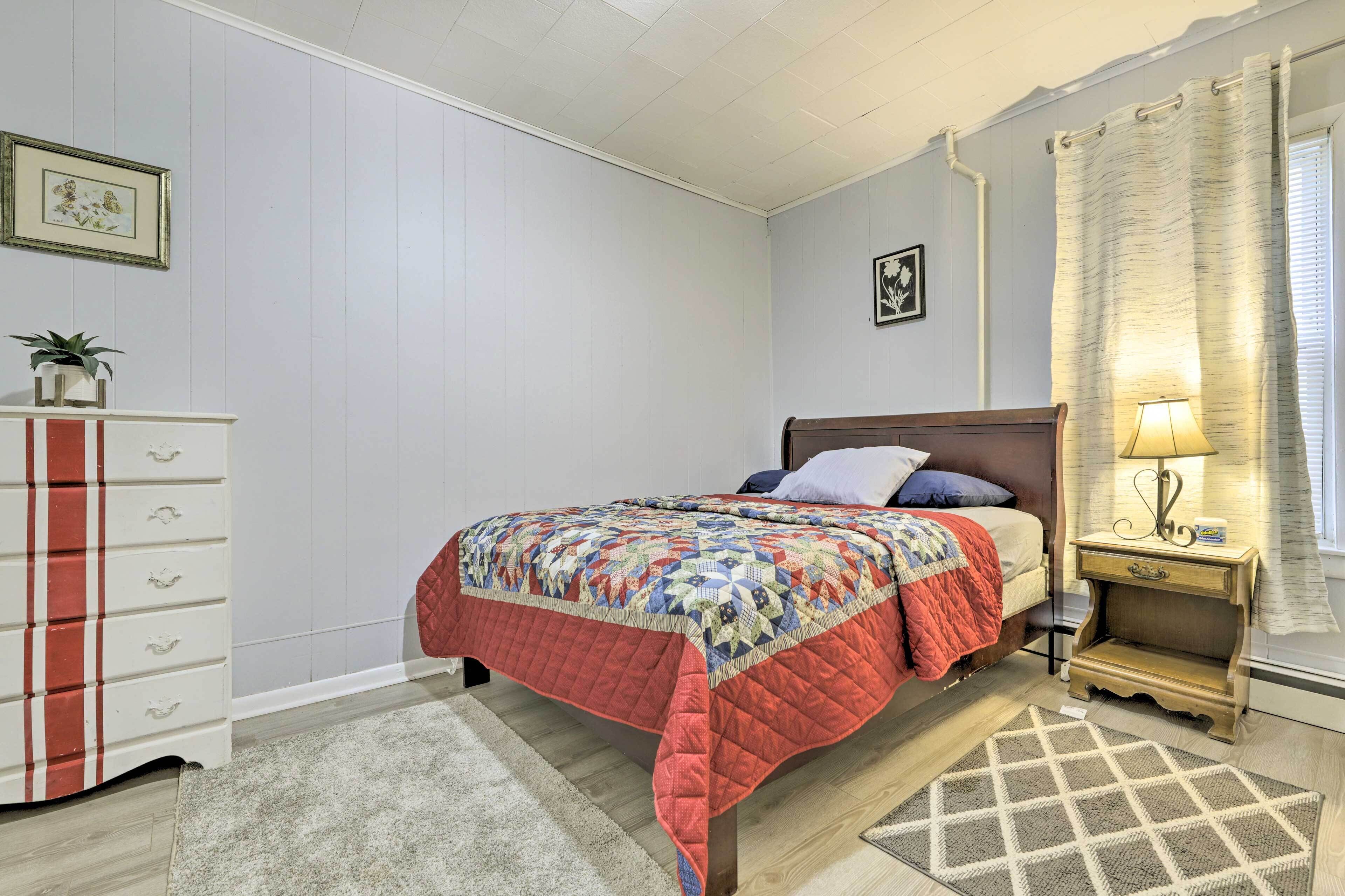A bedroom with a bed, nightstand, dresser, and a window with curtains.