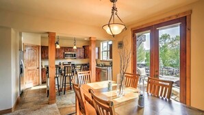 Un vaste espace dédié à la salle à manger, avec une table et des chaises en bois, un luminaire suspendu et une vue sur l’extérieur grâce à de grandes fenêtres.