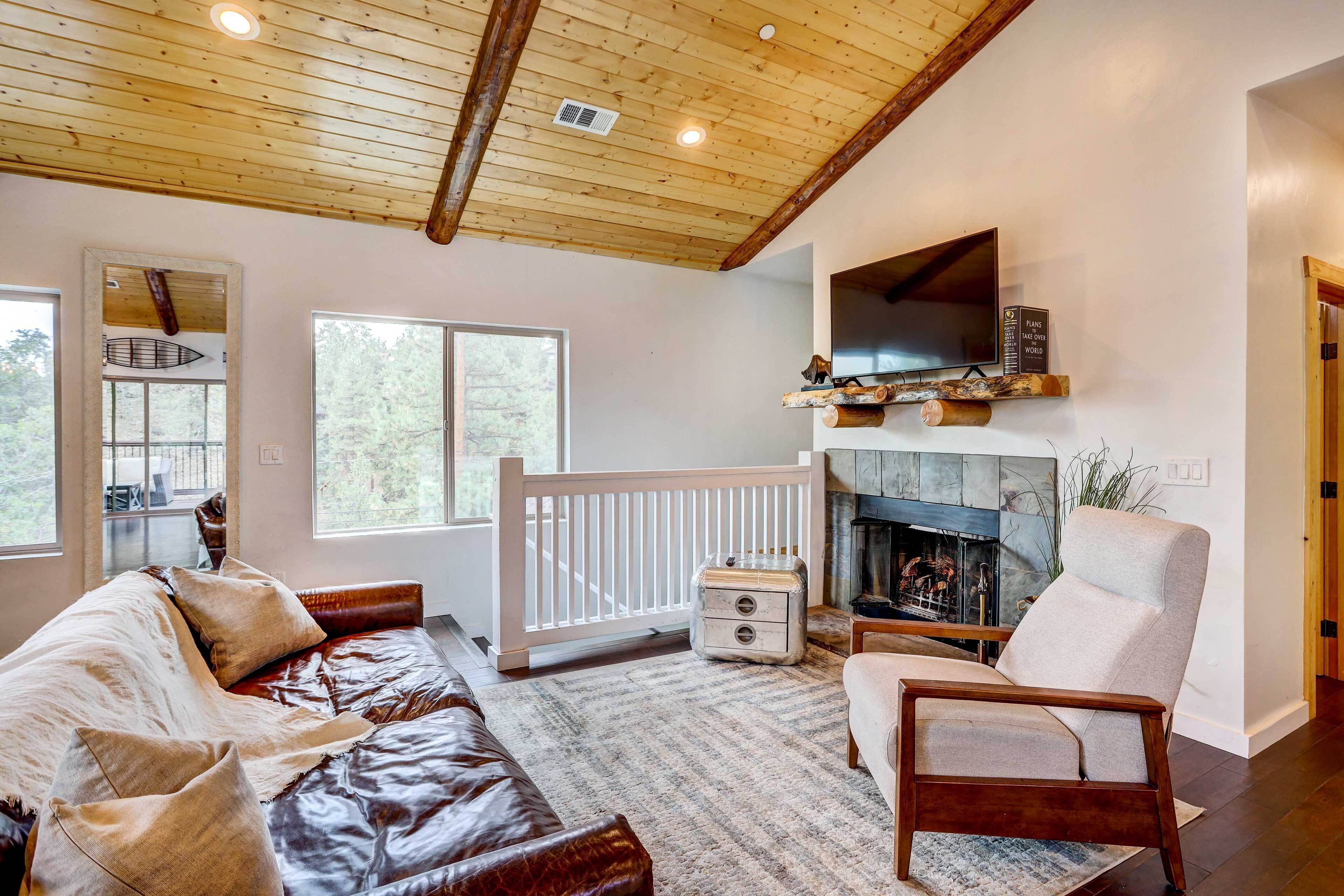 A cozy living room with a wooden ceiling, a fireplace, a TV mounted above it, and a comfortable seating area with a sofa and armchair.