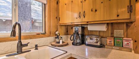 A kitchen with wooden cabinets, a sink, a coffee maker, a toaster, and tea bags on the counter.