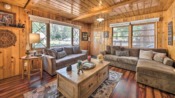 A cozy cabin interior with wooden walls and floors, two sofas, a coffee table, and large windows offering views of the outdoors. - < 3 Mi to Lake: Pet-friendly Big Bear Cabin (Big Bear Lake)