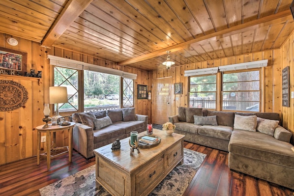 Ein gemütliches Blockhaus-Interieur mit Holzwänden und -böden, zwei Sofas, einem Couchtisch und großen Fenstern mit Blick ins Freie.