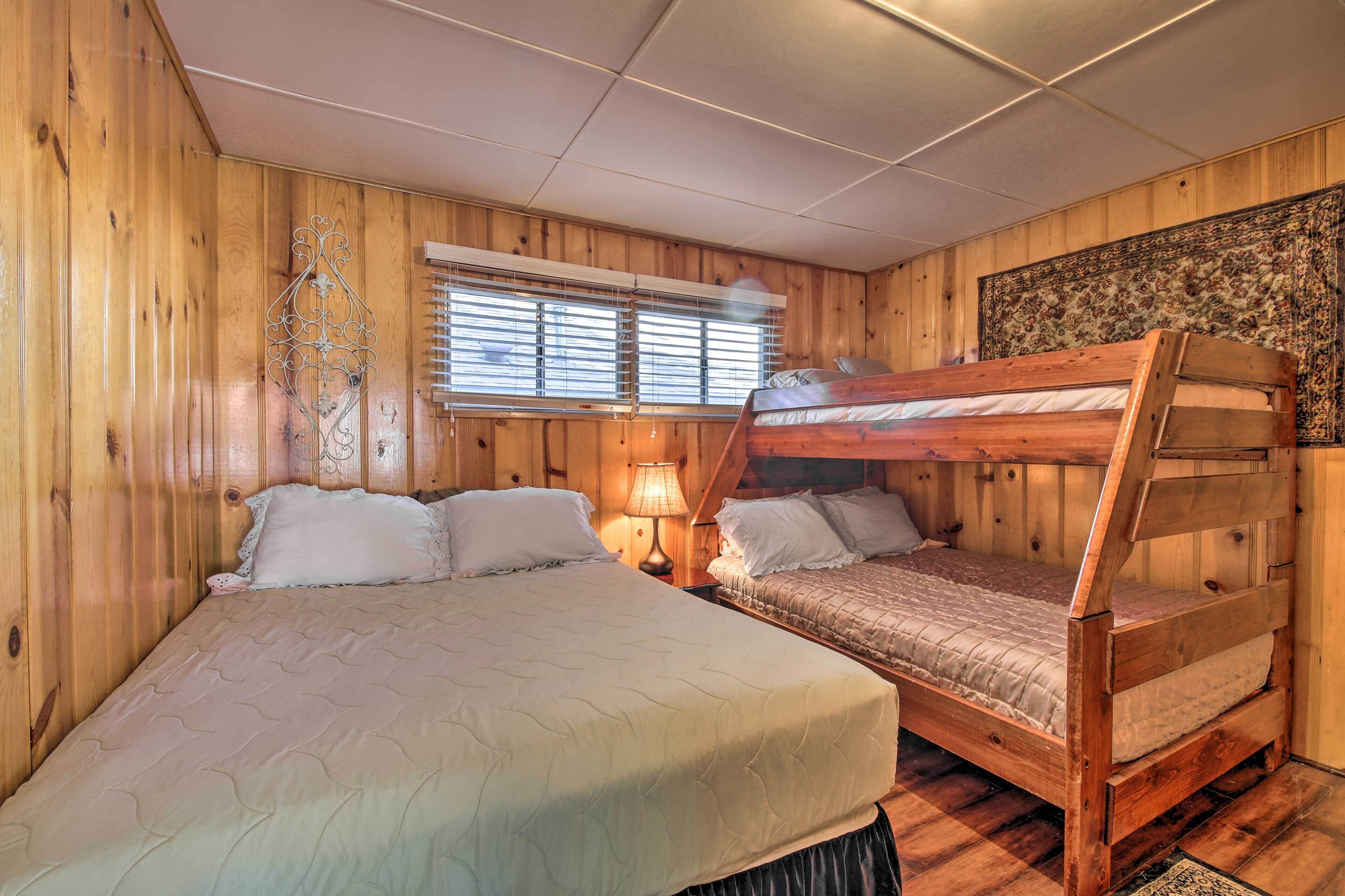 Una habitación de madera con una cama grande, otra más pequeña y una cama nido. Hay una ventana con persianas y un adorno metálico en la pared.