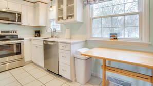 A modern kitchen with white cabinetry, stainless steel appliances, and a wooden table. - 1 Mi to Beach: Quiet West Dennis Escape w/ Sunroom (West Dennis)