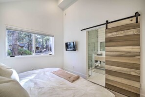 Une chambre avec un lit, une fenêtre donnant sur des arbres, un téléviseur et une porte coulissante ornée de panneaux en bois.