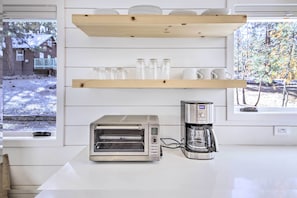 A kitchen with a built-in toaster oven, a coffee maker, and wooden shelves above holding dishes and glasses.
