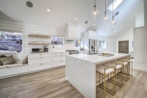 Une cuisine moderne avec des meubles blancs, un grand îlot central doté de tabourets et un éclairage suspendu.