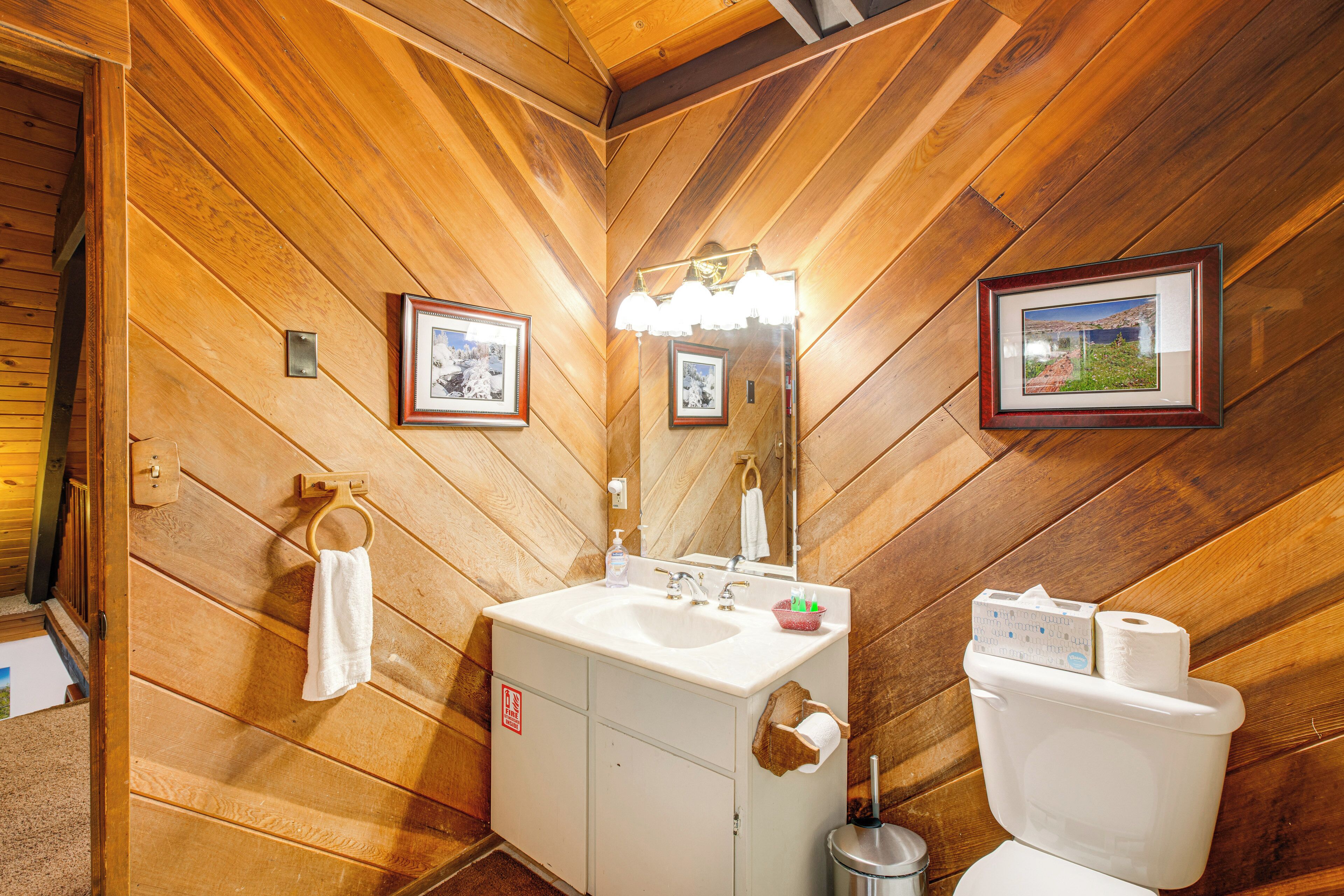 Ein Badezimmer mit Holzwandverkleidung, Waschbecken, Spiegel und Toilette.