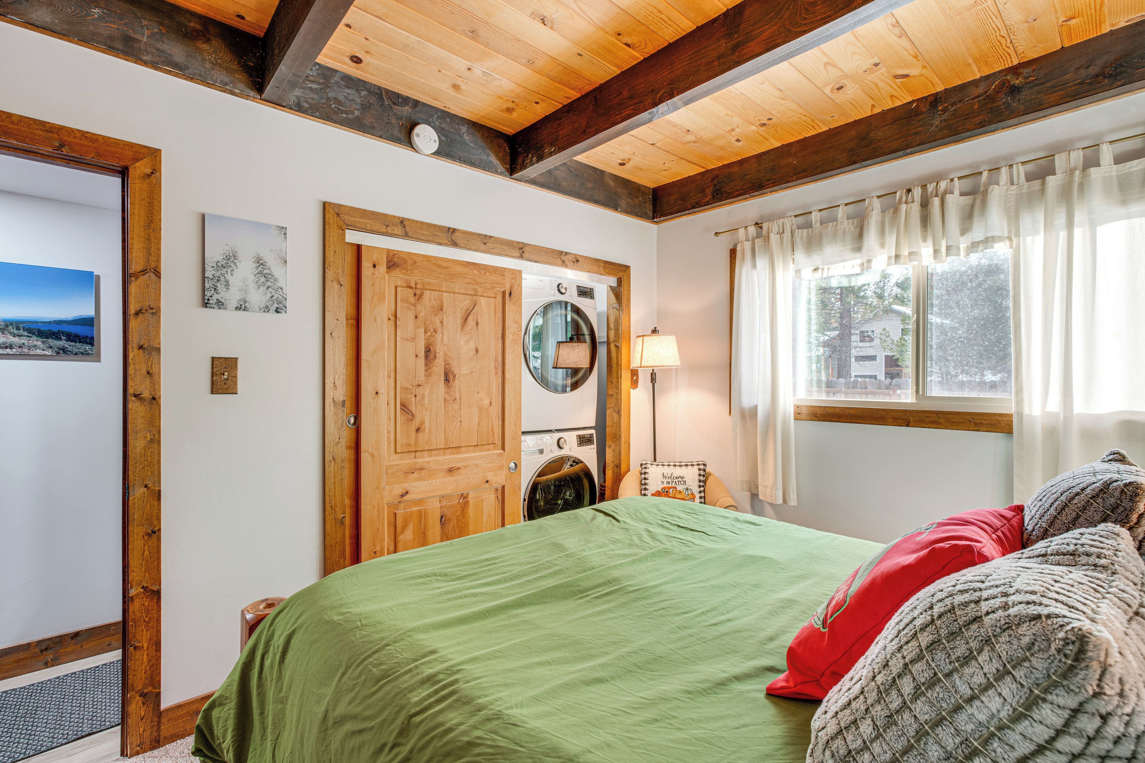 Een kamer met een bed, een houten deur, een wasmachine en een raam met gordijnen.