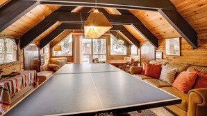 A cozy room with a ping pong table, wooden beams, and a sofa with cushions.