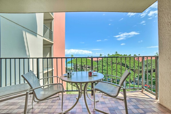 A balcony with a table and two chairs, overlooking a lush green landscape and a clear blue sky.