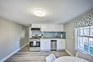 A modern kitchen with white cabinets, stainless steel appliances, and a window with patterned valance.