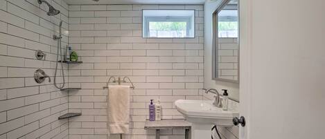 Une salle de bain avec des murs carrelés de carreaux blancs, une douche, une fenêtre, un lavabo et un porte-serviettes.