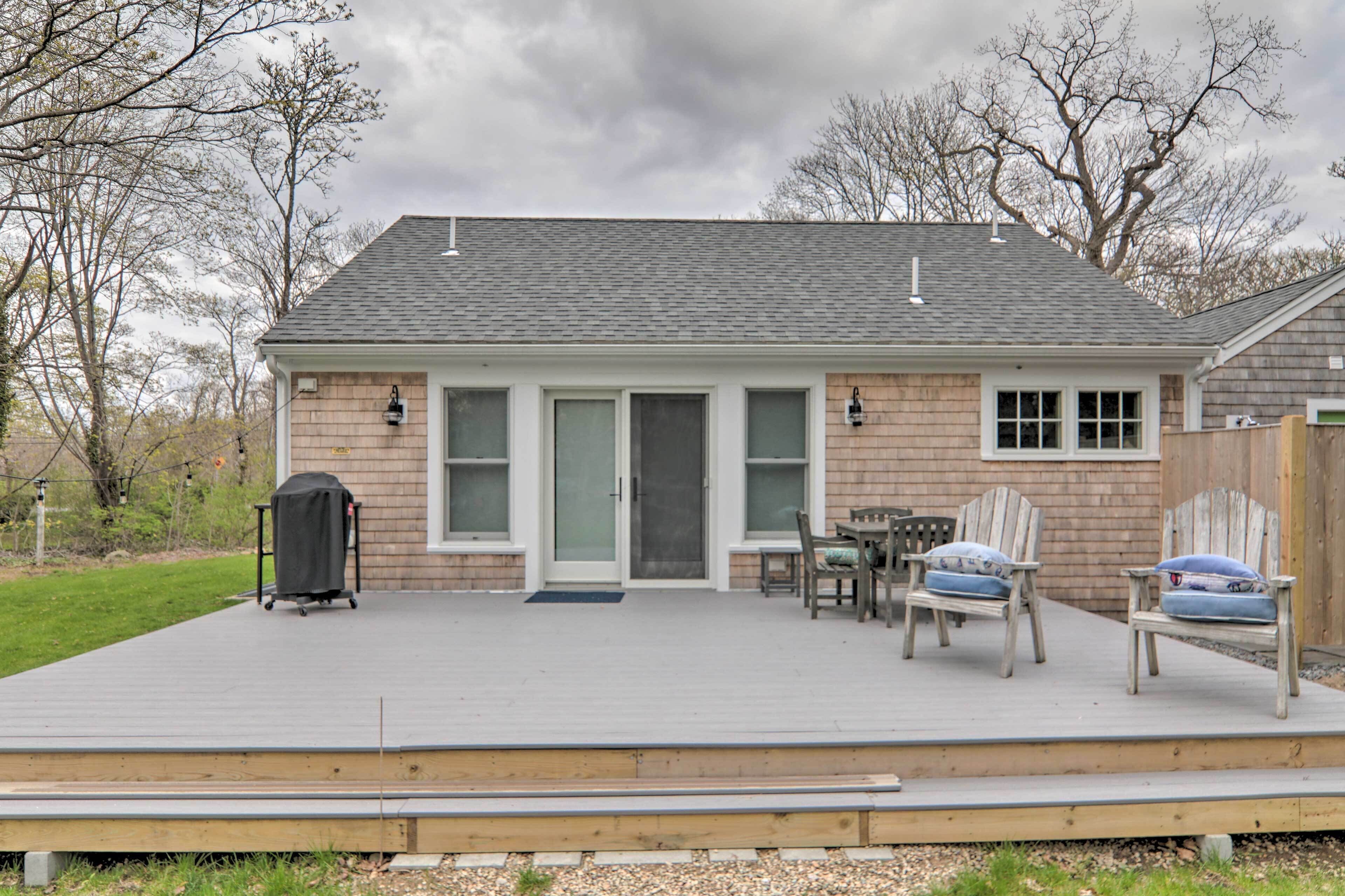 A house with a covered deck, two wooden chairs, a table, and a barbecue grill.